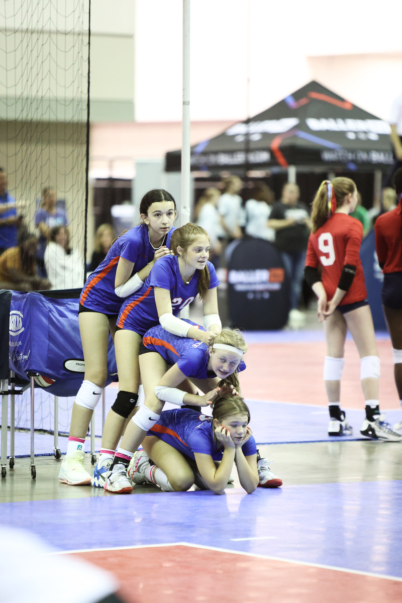 Four girls leaning on top of each other watching a match