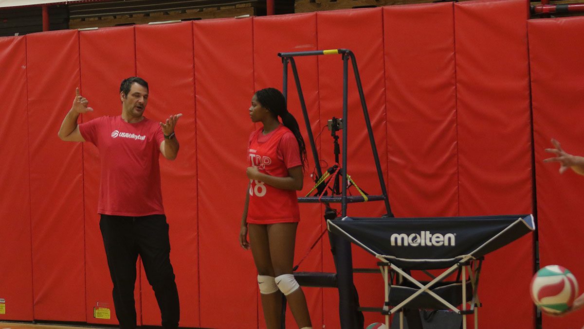A male coach works with a female athlete on serving